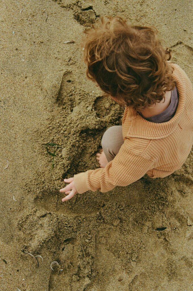Son of documentary family photographer plays in the sand, cute curls blowing in the sea air