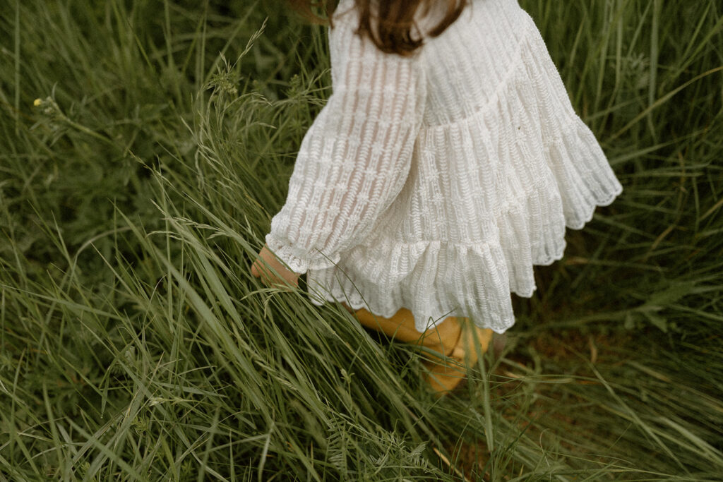 Close-up of a child’s textured white dress moving through tall grass, highlighting the soft fabrics often chosen for what to wear for family photos.