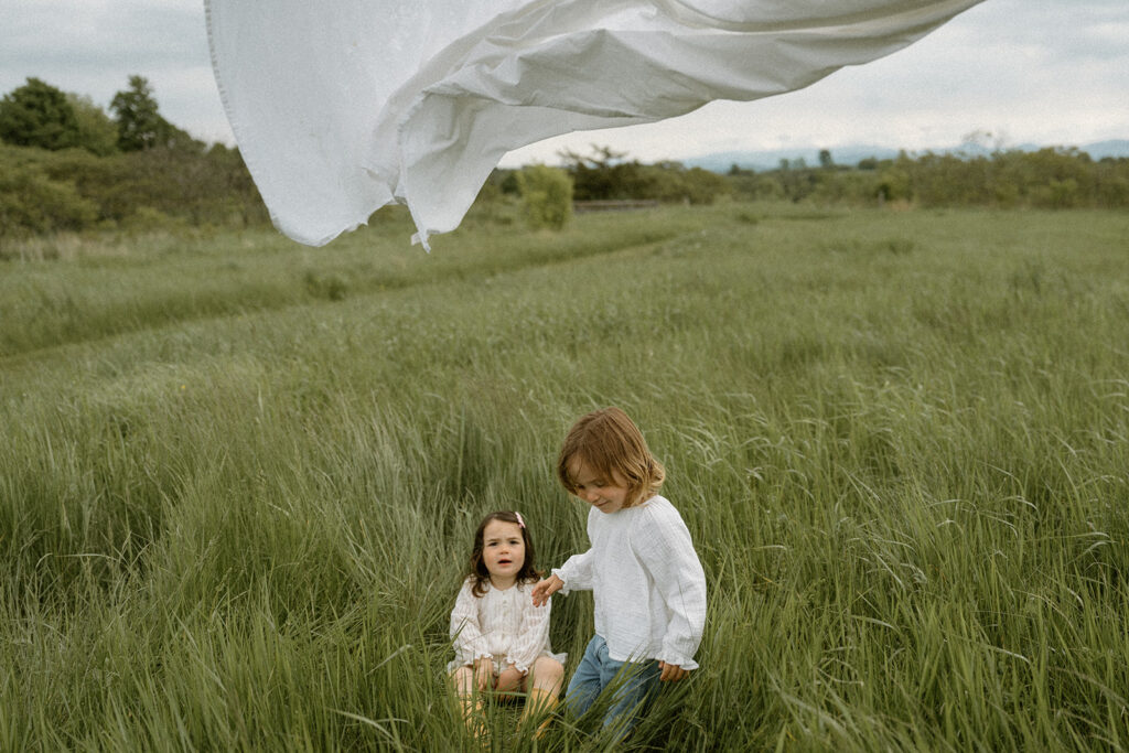 Two children standing in tall grass during a golden hour field session, illustrating a soft natural family photos color scheme that complements the Vermont landscape.