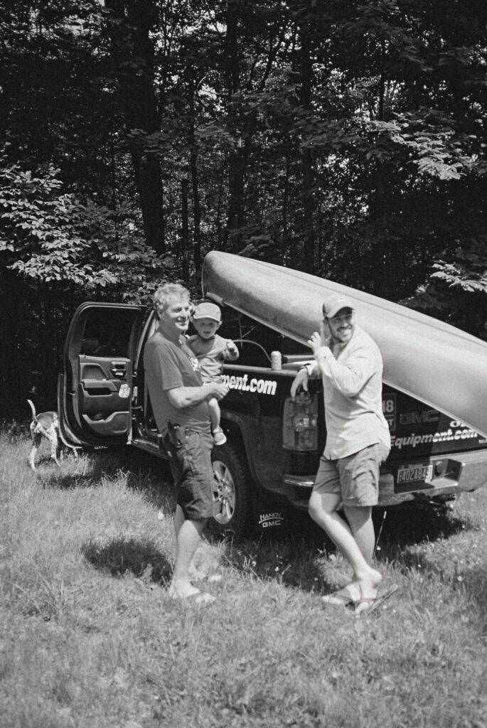 Three generations of men lean on truck before going canoeing