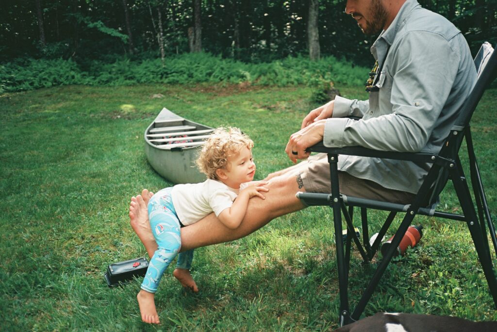 Toddler lays sprawled on his dad's legs after a canoe excursion