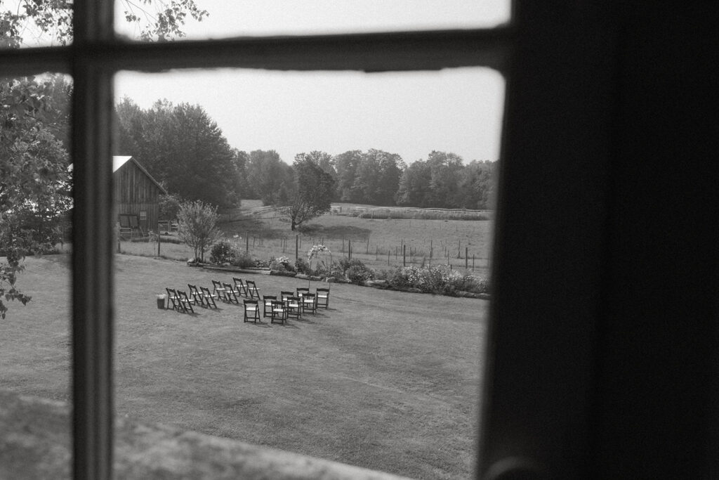 Black and white view of a small outdoor wedding ceremony through a farmhouse window in rural Vermont.