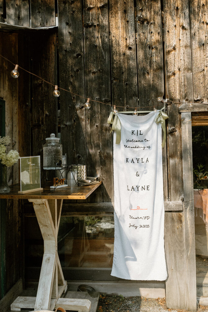 Hand embroidered welcome banner hanging on a rustic barn door at a small Vermont wedding celebration.