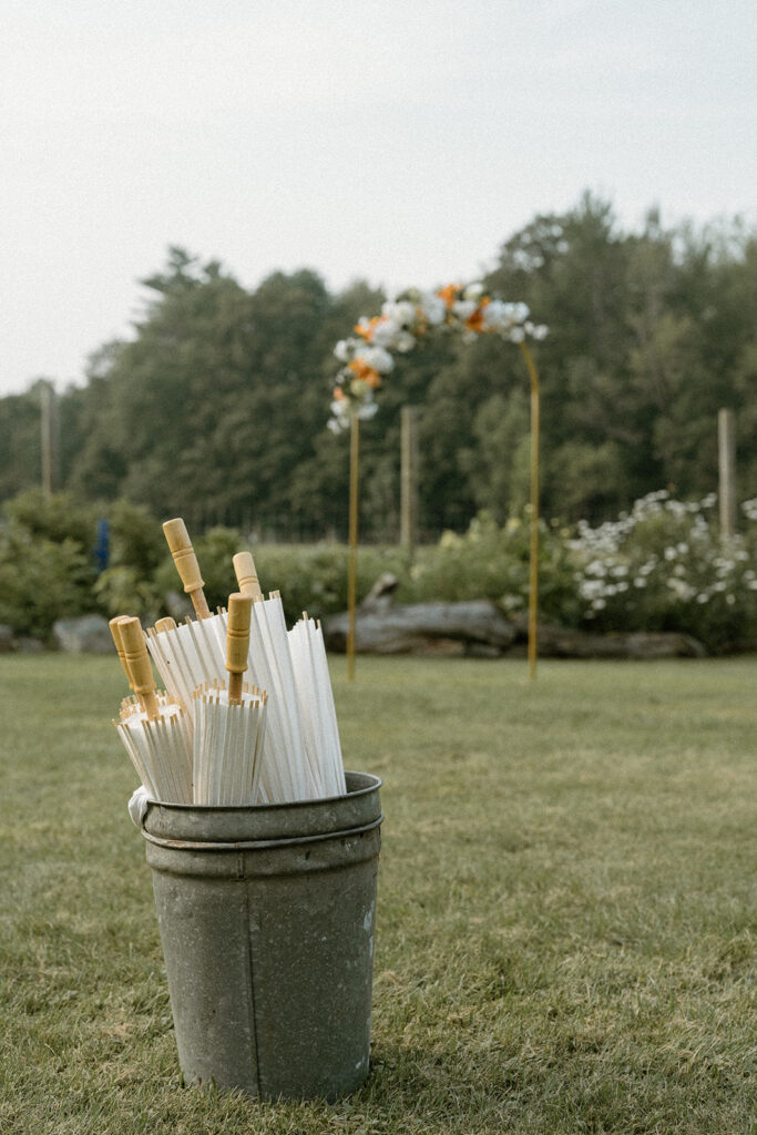 Metal bucket filled with paper parasols for guests at an outdoor ceremony at an intimate wedding location in Vermont.