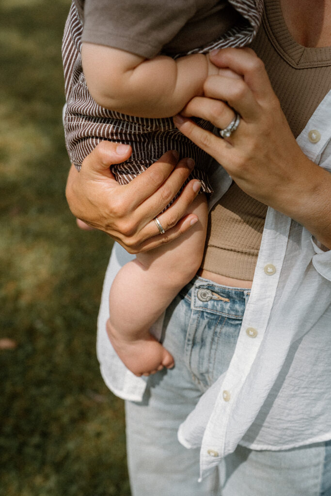 Close-up detail of mother holding baby in arms during warm golden hour summer family photos in Vermont.