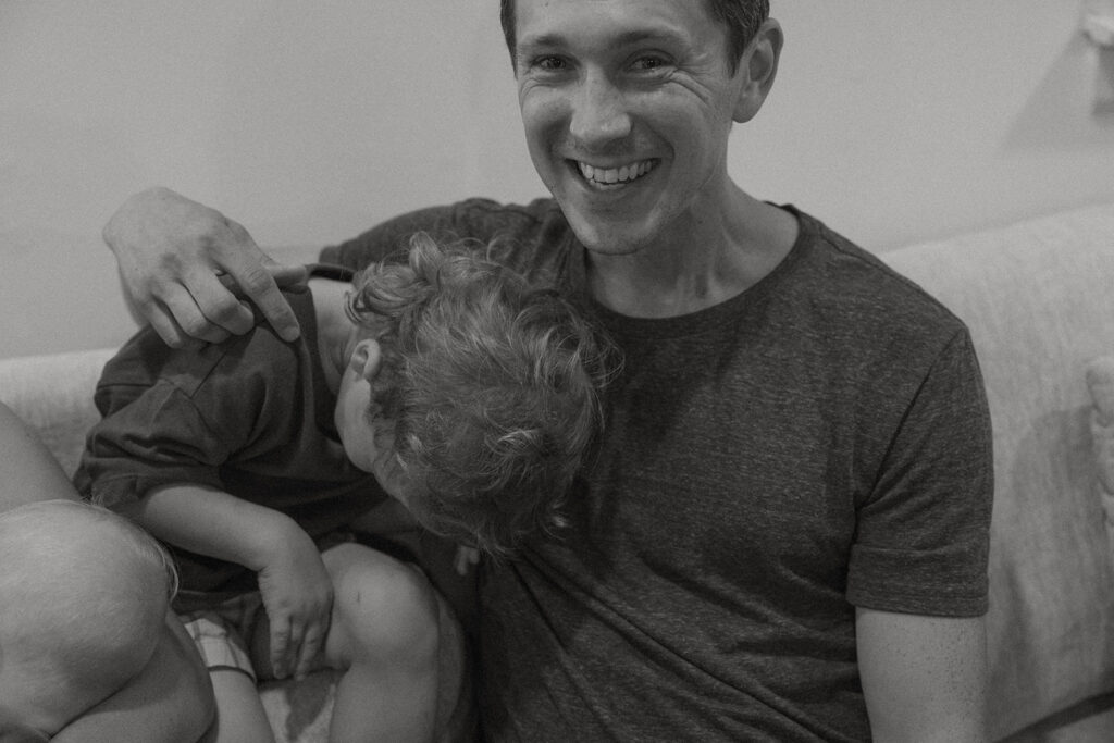 Father smiling while toddler cuddles beside him.