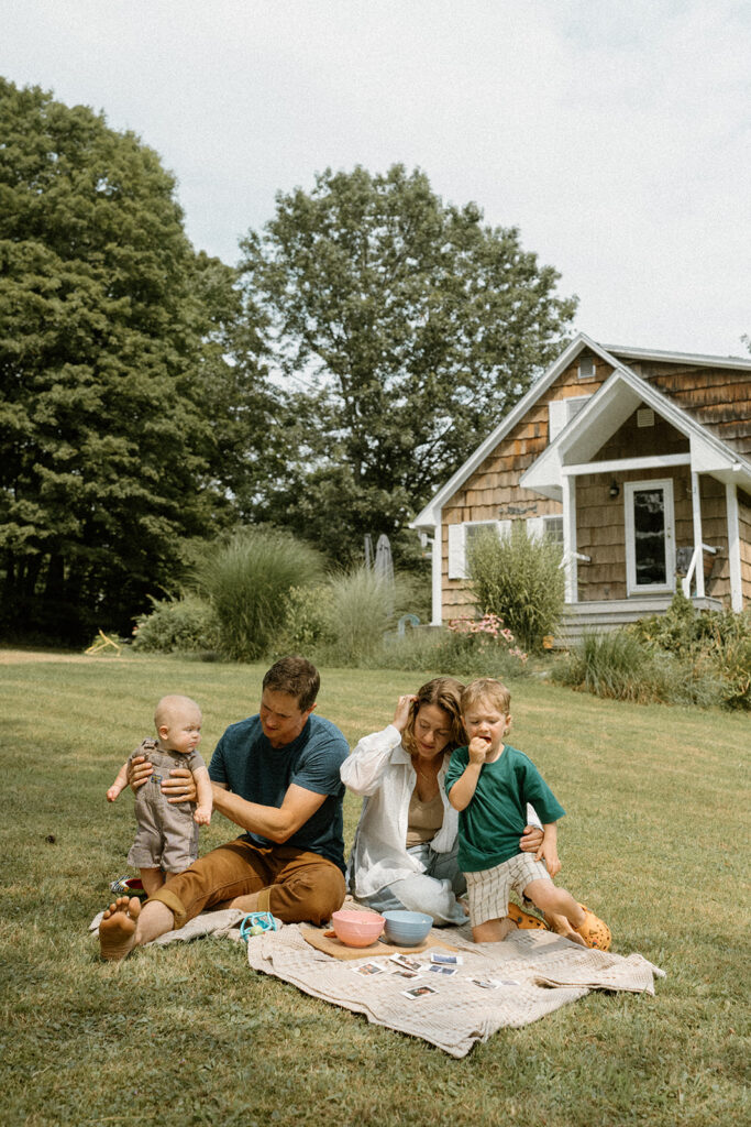 Family sitting on a blanket in the backyard sharing snacks and looking through Polaroid photos