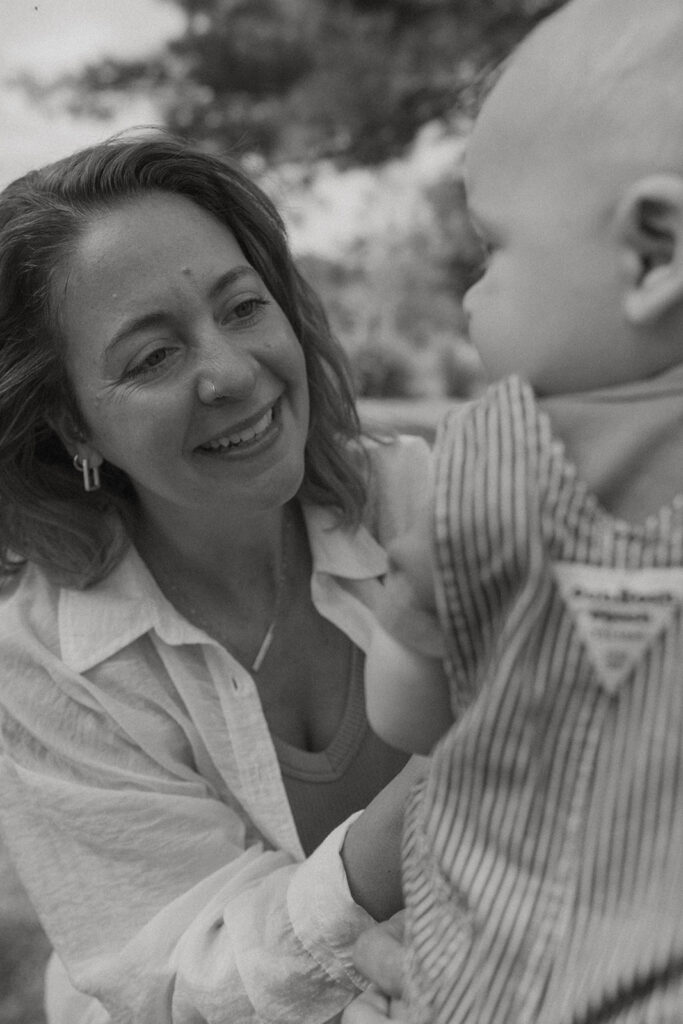 Black and white close-up of mother smiling at baby during intimate lifestyle family photos outdoors.