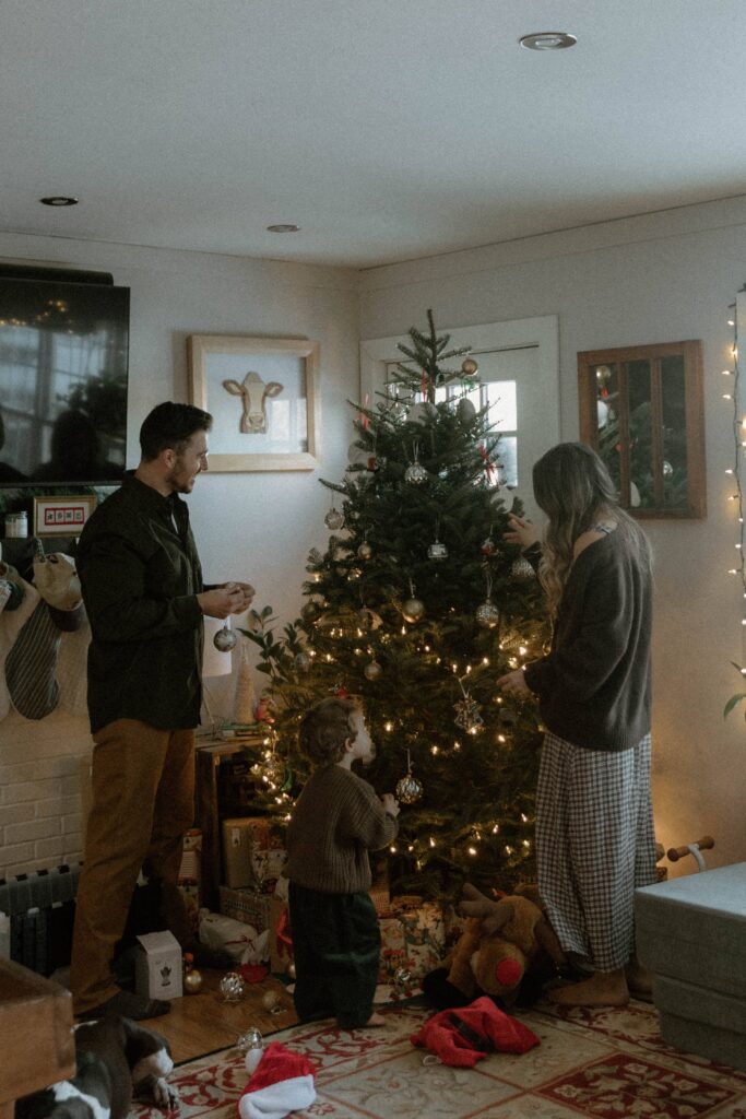 Family decorating their Christmas tree together in a cozy home, photographed by a Vermont family photographer with soft neutral outfits styled to feel natural and timeless.