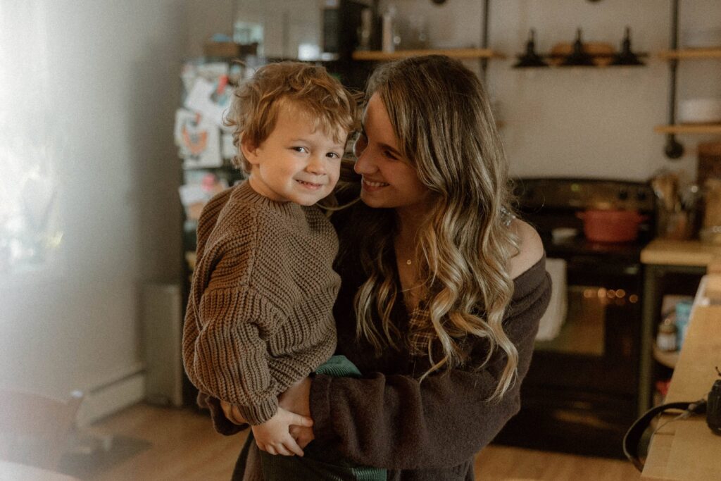 Mother holding her toddler in a cozy kitchen moment, showing a natural example of what to wear for family photos with soft knit textures and earthy tones styled for a Vermont family photographer session.