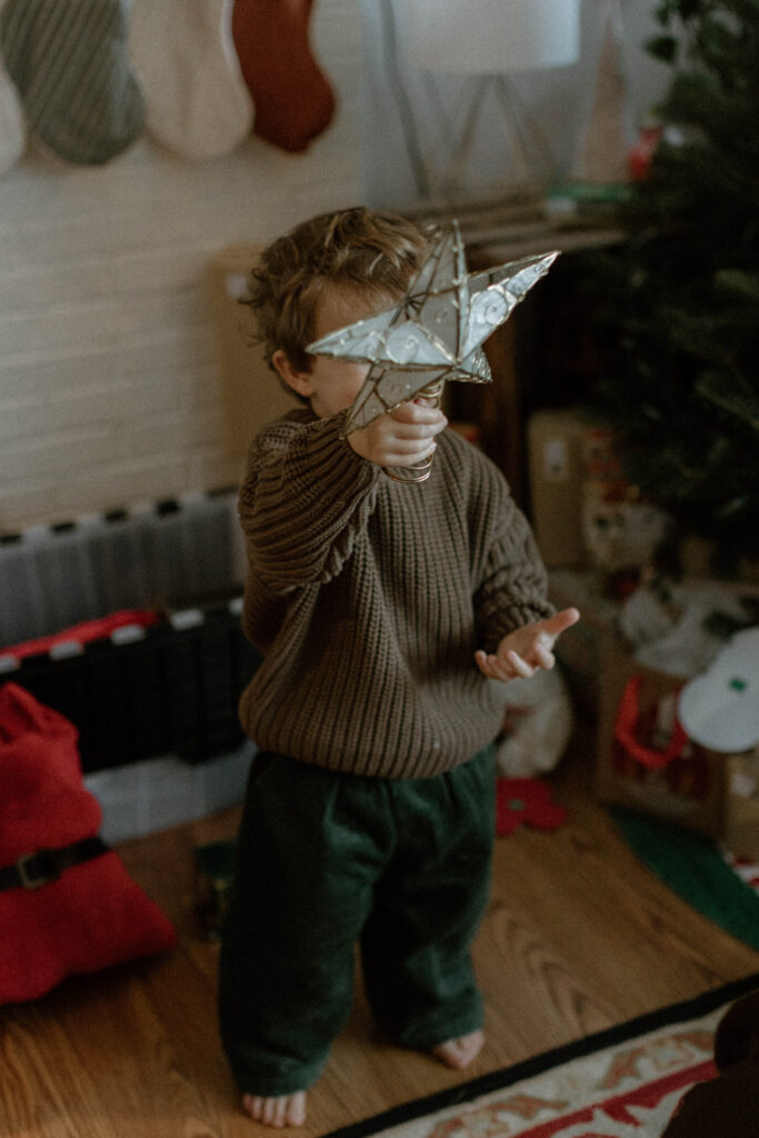 Toddler in a chunky brown sweater and green pants playing with a star ornament, a candid example of comfortable family photo outfits that allow kids to move naturally.