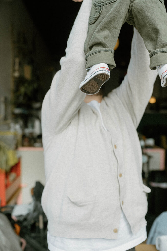 Father lifting his baby in the air while wearing neutral knit layers, a candid moment showing how comfortable clothes help when you dress for family photos with movement in mind.