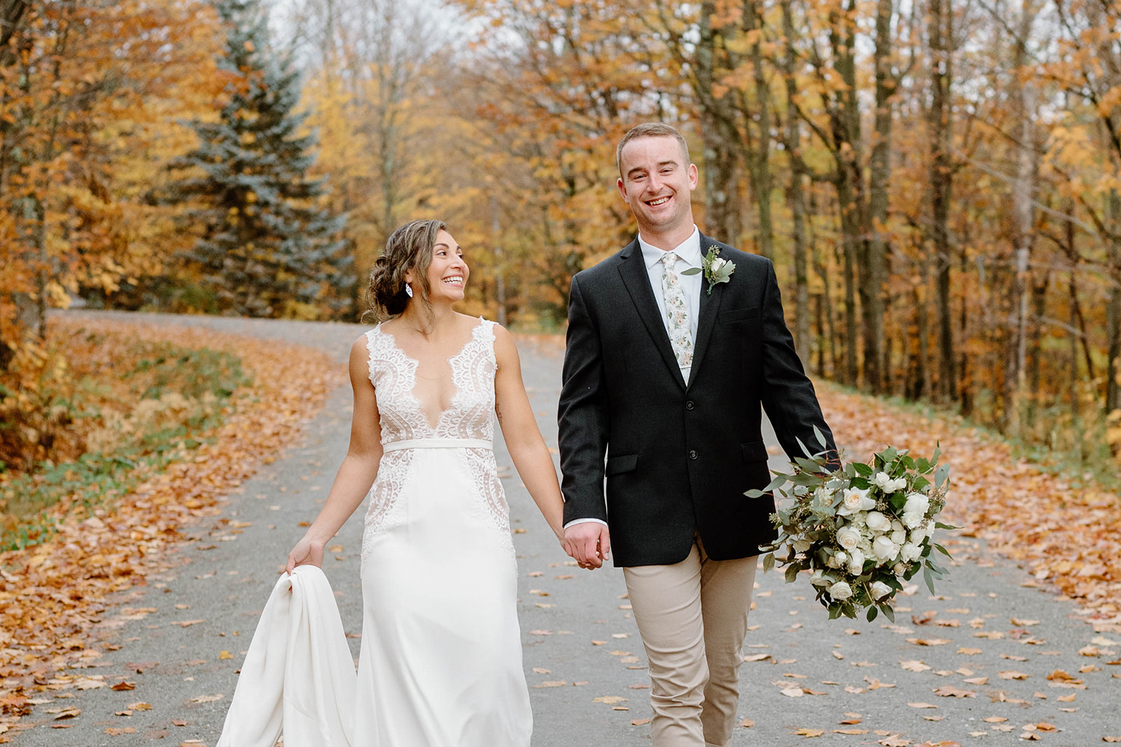 bride and groom smiling while walking along autumn trail at Jay Peak Resort in Jay, Vermont