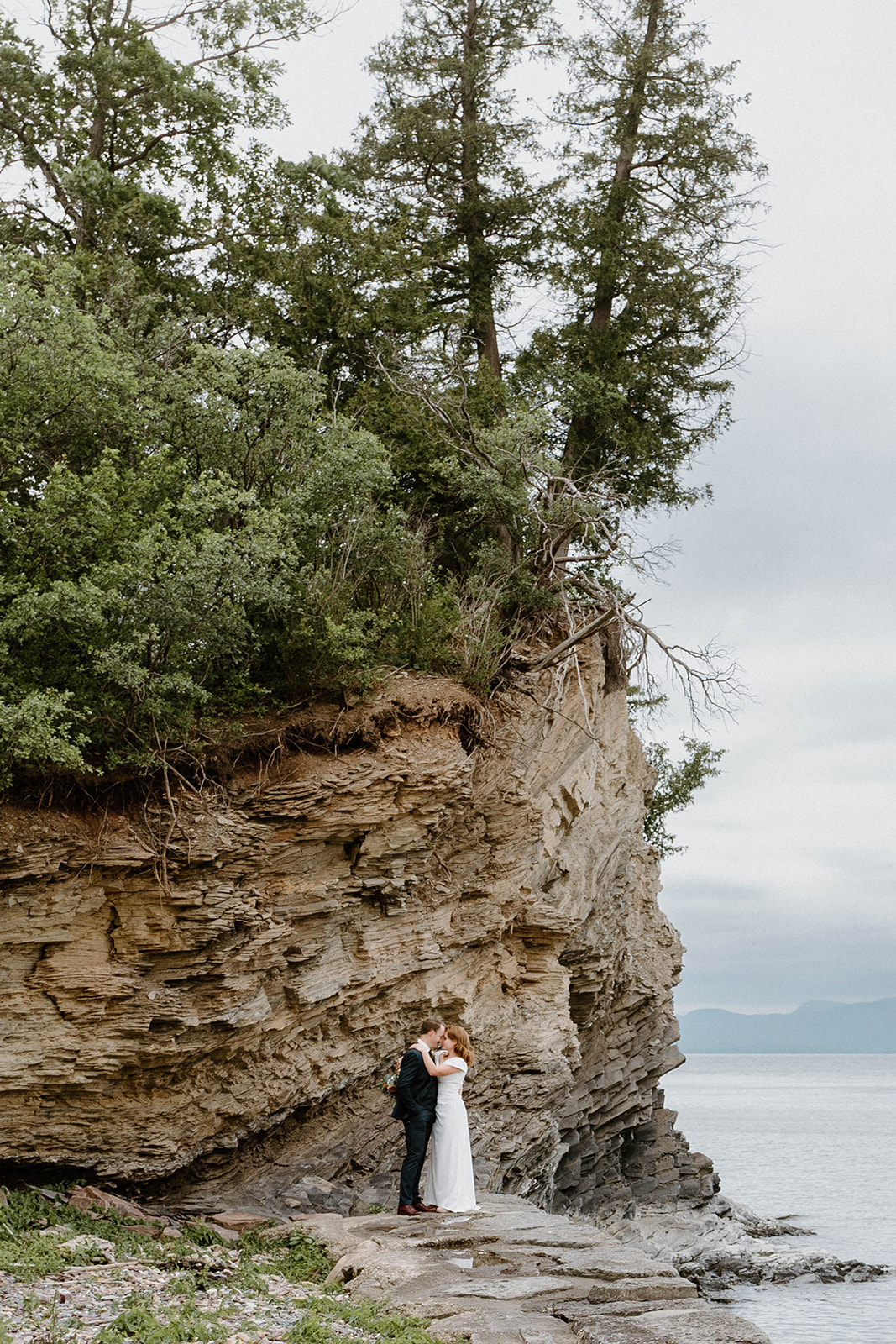 bride and groom kissing under cliff at Shelburne Farms in Vermont