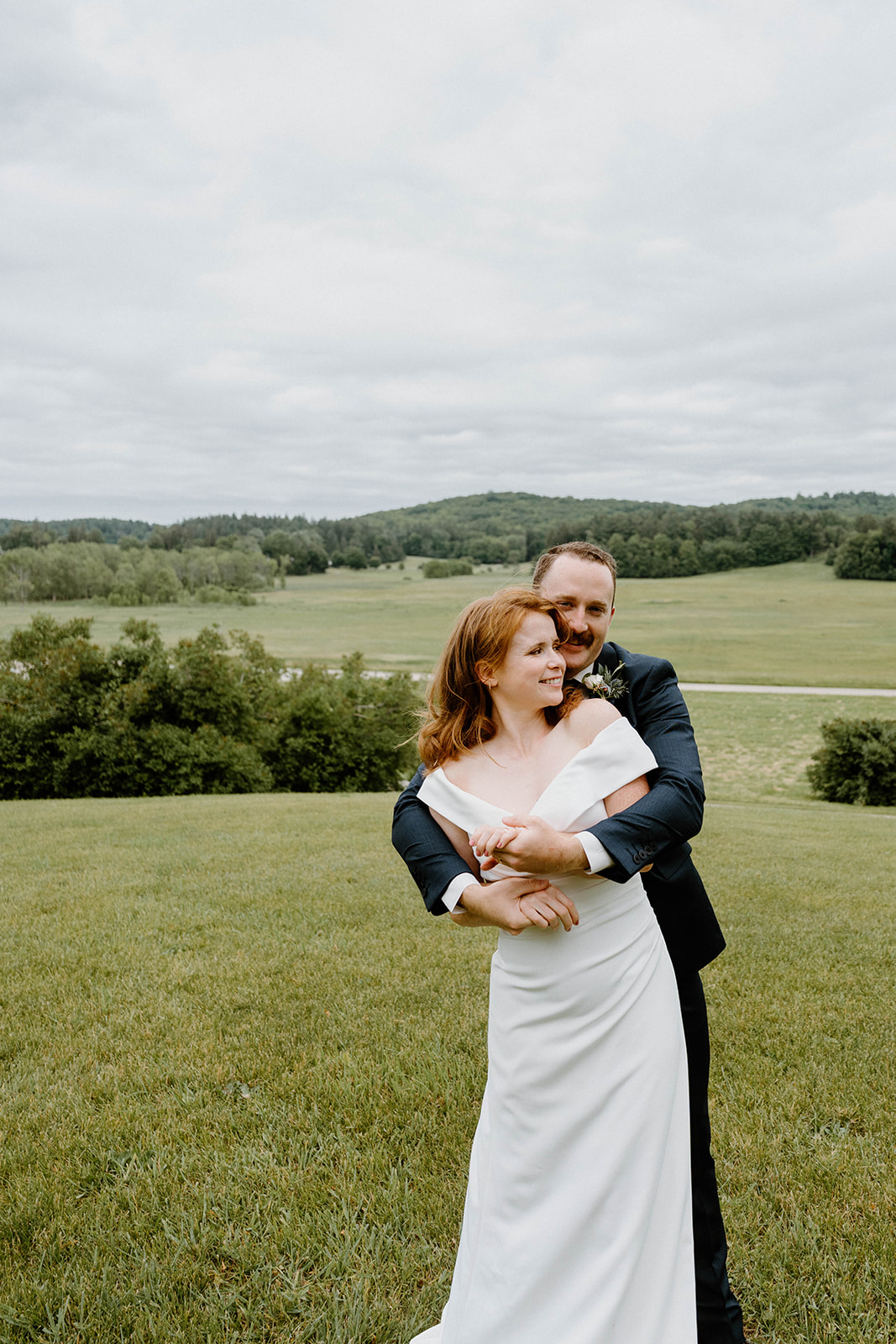groom smiling with arms around bride overlooking view of Shelburne Farms in Vermont