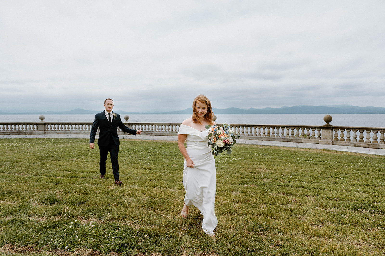 candid shot of bride and groom in grass near the water at Shelburne Farms in Vermont