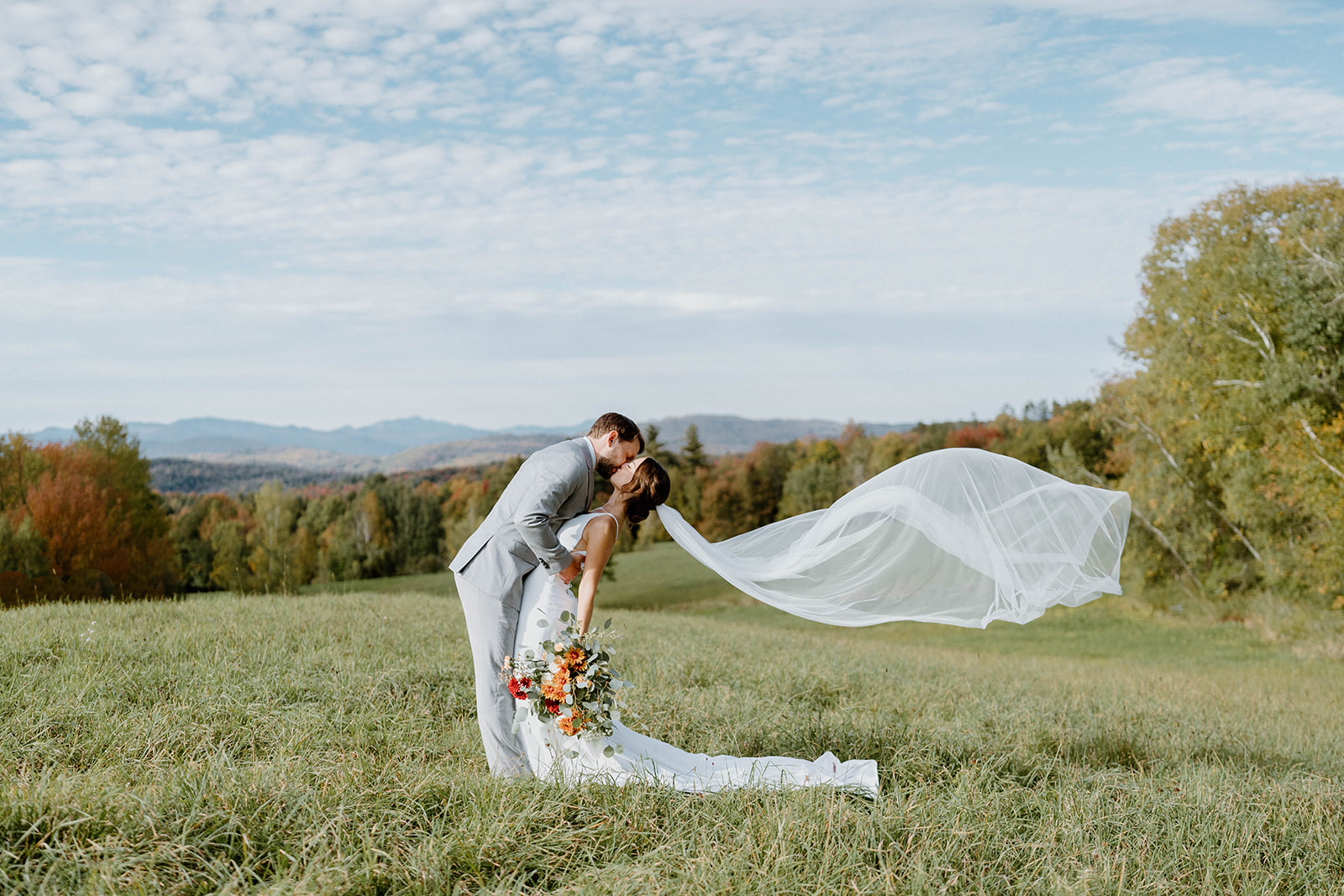 bride and groom kissing in field with scenic mountain view at Bliss Ridge Farm in Moretown, Vermont