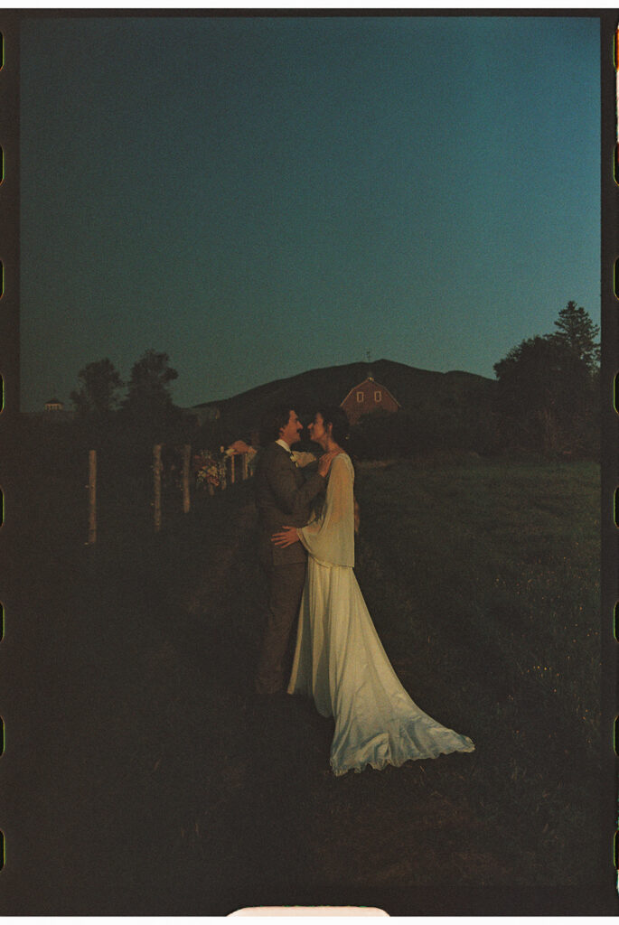 Newlywed couple embracing at dusk in a grassy Vermont field after their ceremony at one of the state’s most romantic intimate wedding locations.