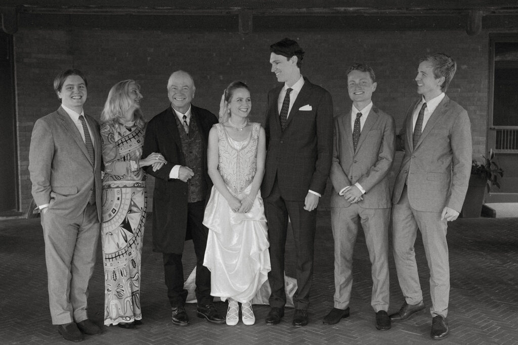 Bride and groom standing with family members in classic black-and-white portrait during historic Brick House wedding at Shelburne Museum in Vermont.