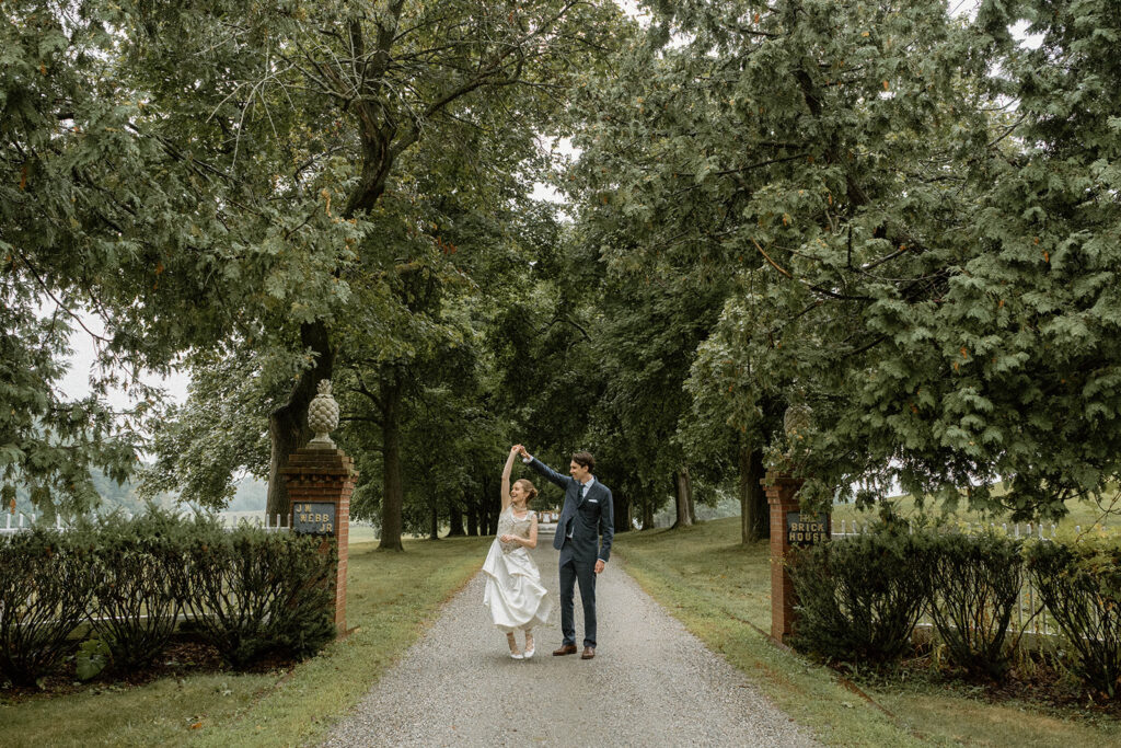 Bride and groom dancing together on the tree-lined driveway leading to the Brick House during an intimate Vermont wedding celebration.