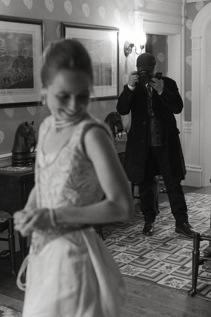 Father photographing bride in heirloom dress inside historic Shelburne Museum home during Vermont wedding morning.