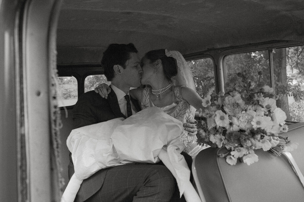 Newlyweds sharing a kiss in the back of a vintage car after their Shelburne Museum wedding in Vermont.