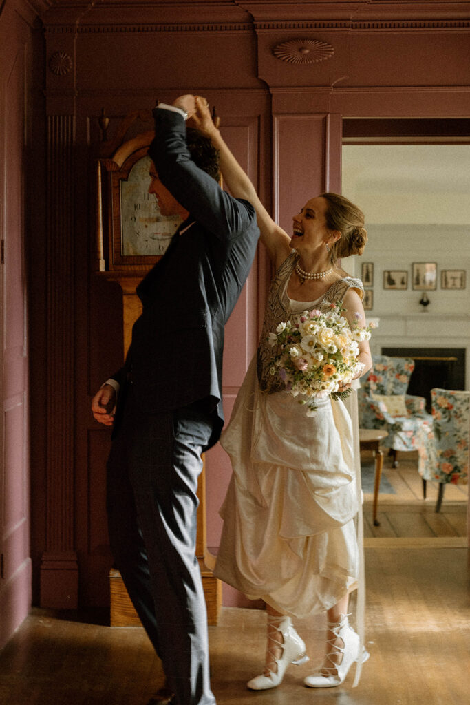Bride twirling groom while holding bouquet inside the historic Brick House at Shelburne Museum wedding reception in Vermont.