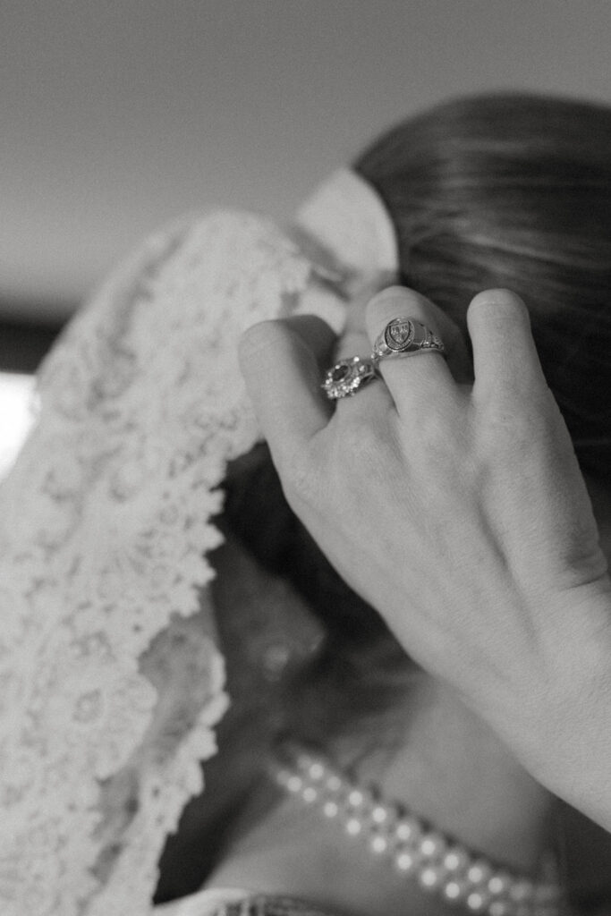 Bride adjusting heirloom veil while wearing vintage diamond rings and pearl necklace during legacy wedding at Brick House in Shelburne, Vermont.
