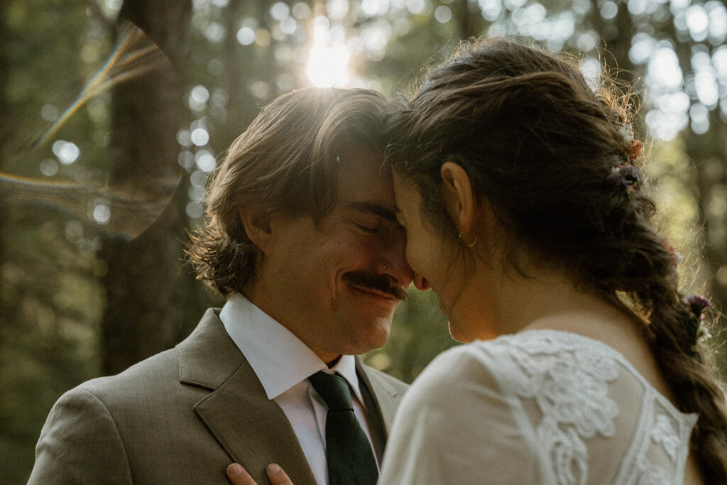 Close-up of bride and groom touching foreheads beneath sunlit trees during a Vermont elopement photographed by a documentary-style elopement photographer.