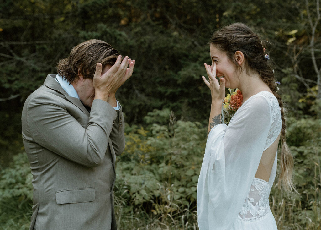 Bride and groom sharing a tearful laugh during their first look in the woods at a secluded Vermont wedding venue.
