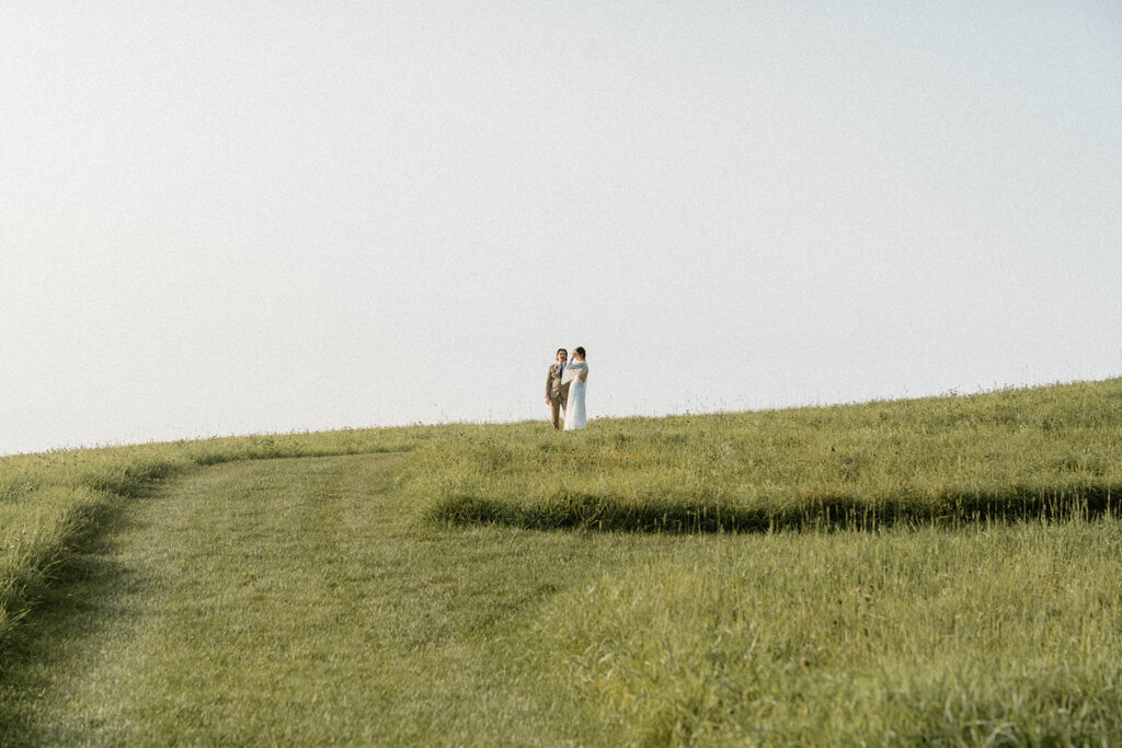 Bride and groom walking across a rolling green hill during their Vermont elopement at a quiet countryside intimate wedding location.