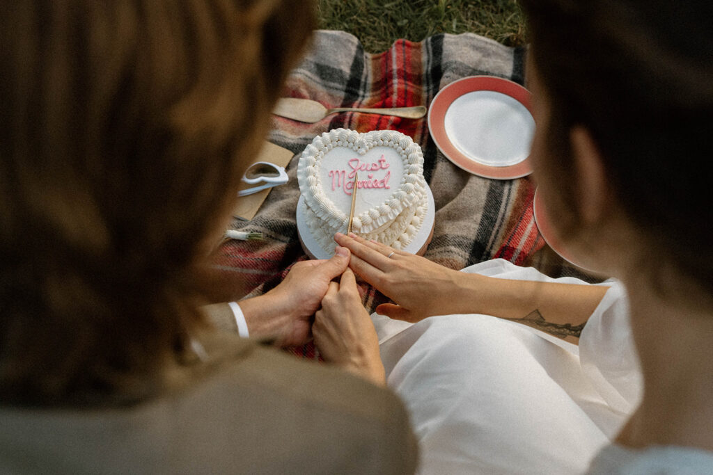 Couple cutting a heart-shaped “Just Married” cake from Red Poppy Cakery during their intimate Vermont elopement picnic.
