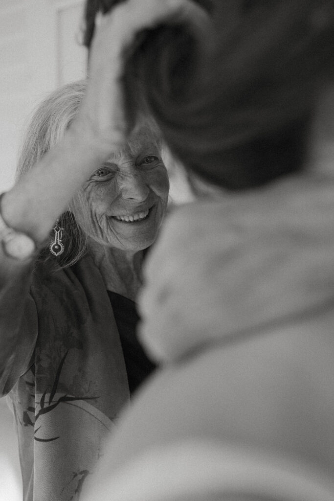 Grandmother smiling at bride while helping adjust veil during emotional getting-ready moment at backyard wedding in Greensboro, Vermont.