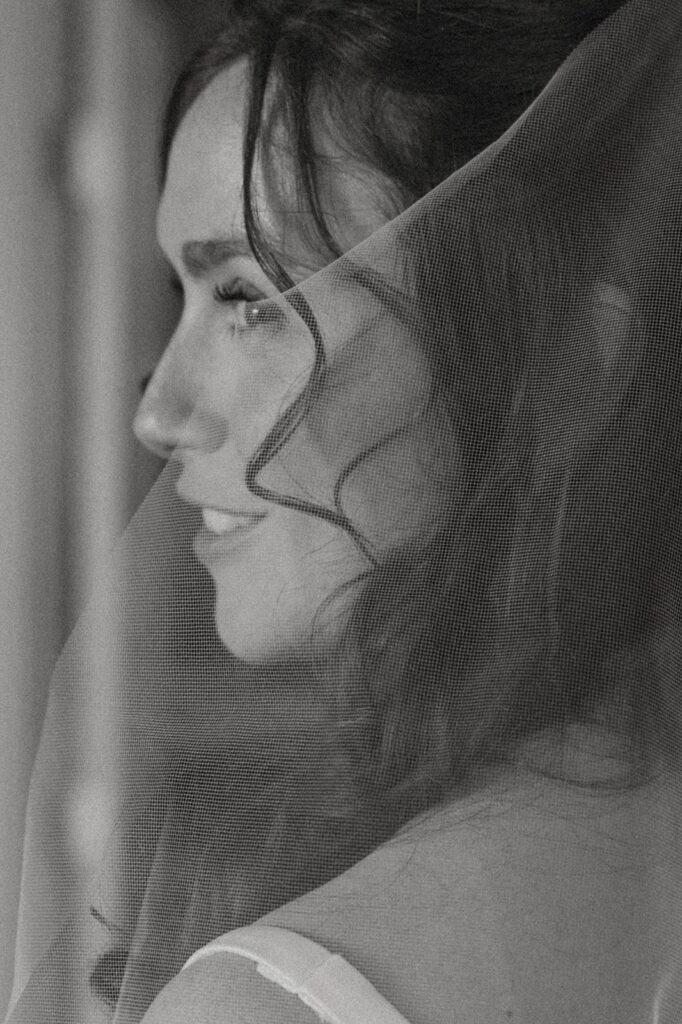 Close-up black and white portrait of a bride smiling softly through her veil.