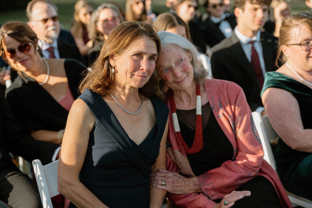 Mother leaning into grandmother during emotional ceremony moment at outdoor Vermont backyard wedding in Greensboro.